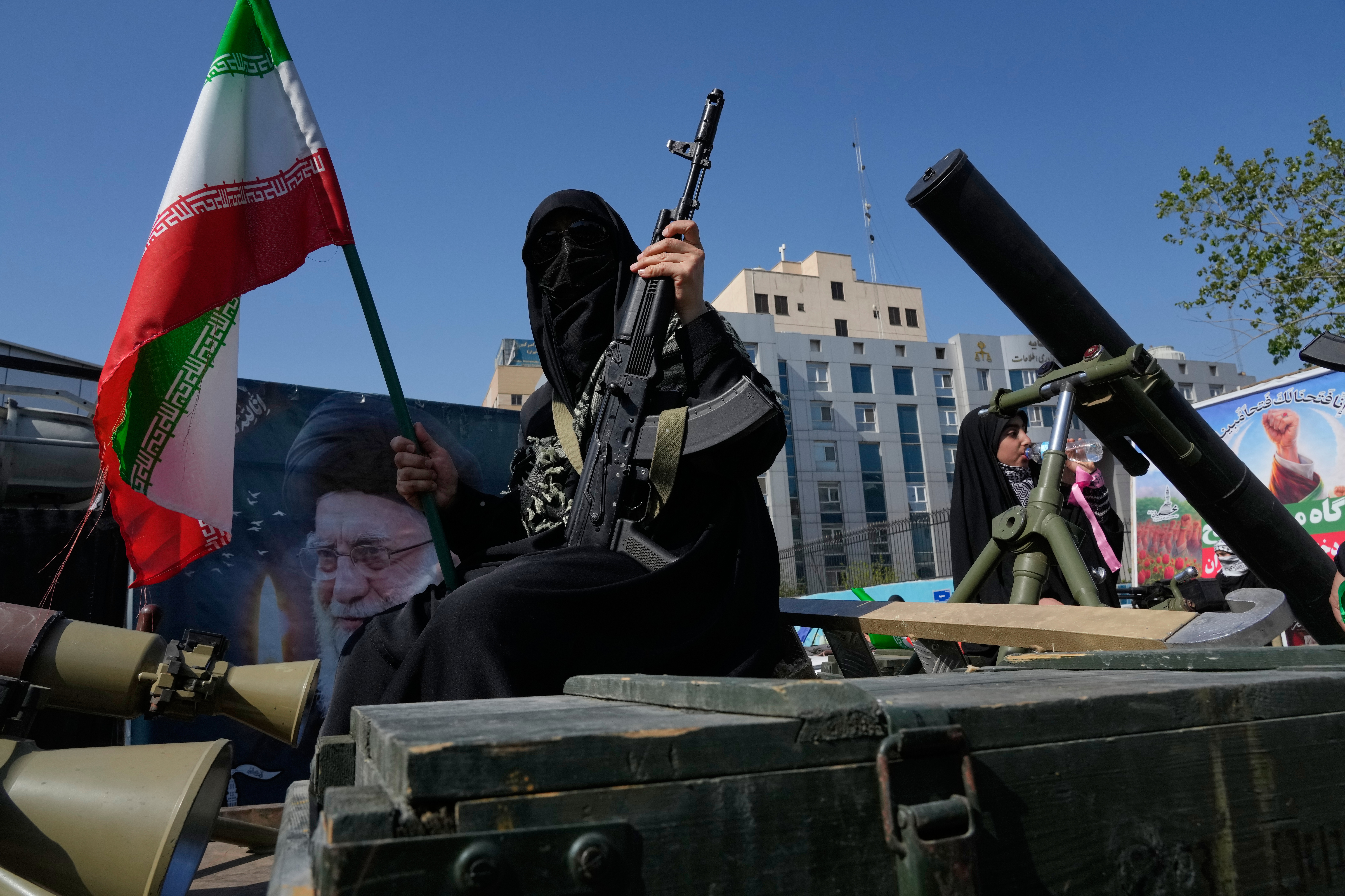 A woman member of the Basij paramilitary, affiliated with Iran's Revolutionary Guard, holds her gun and an Iranian flag during a state-organized rally in support of the supreme leader marking National Girl's Day in Tehran, Iran, on April 17, 2026. 